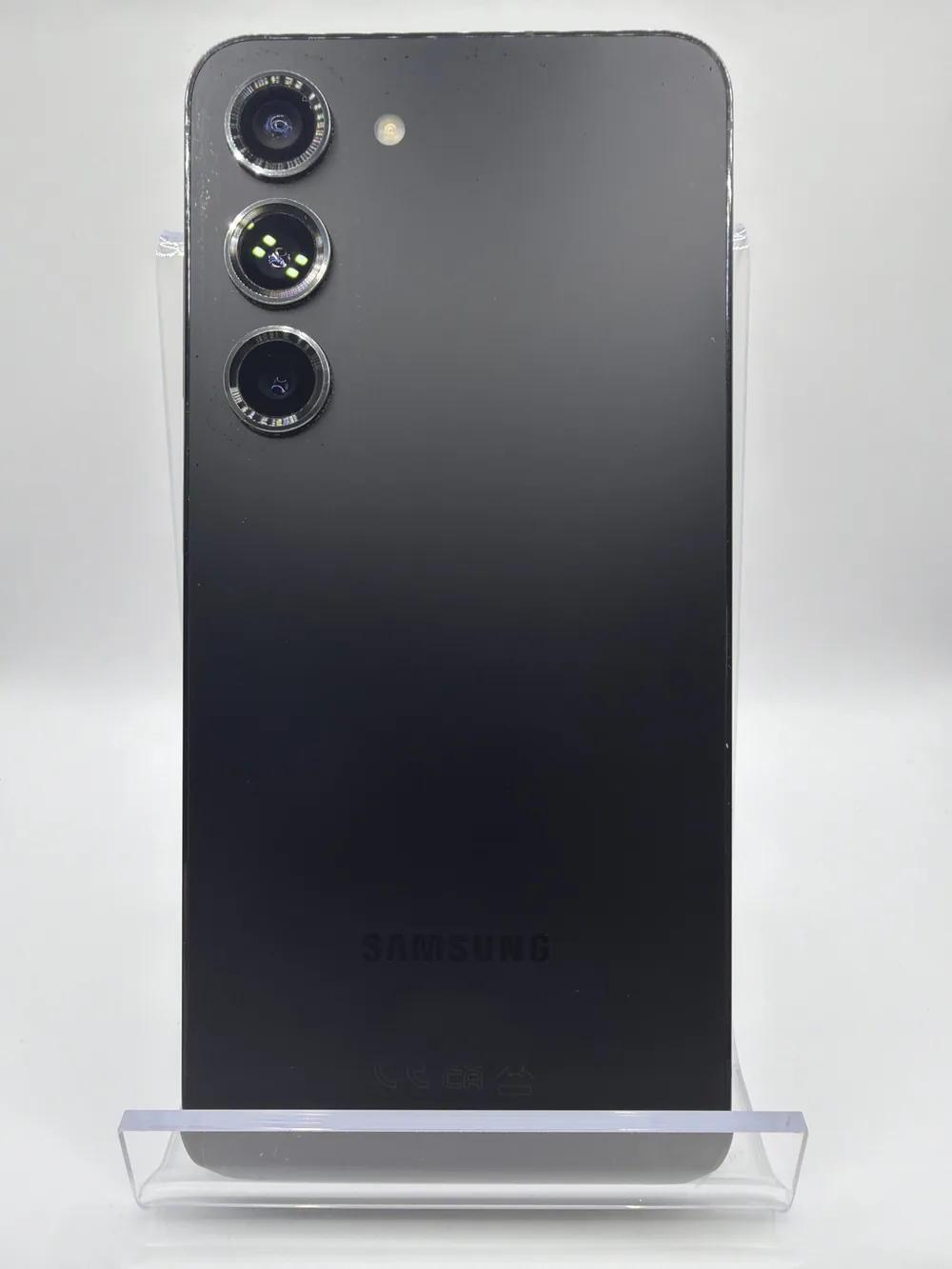 Samsung Galaxy S23 noir, vu de dos, trois capteurs photo alignés, posé sur un support transparent